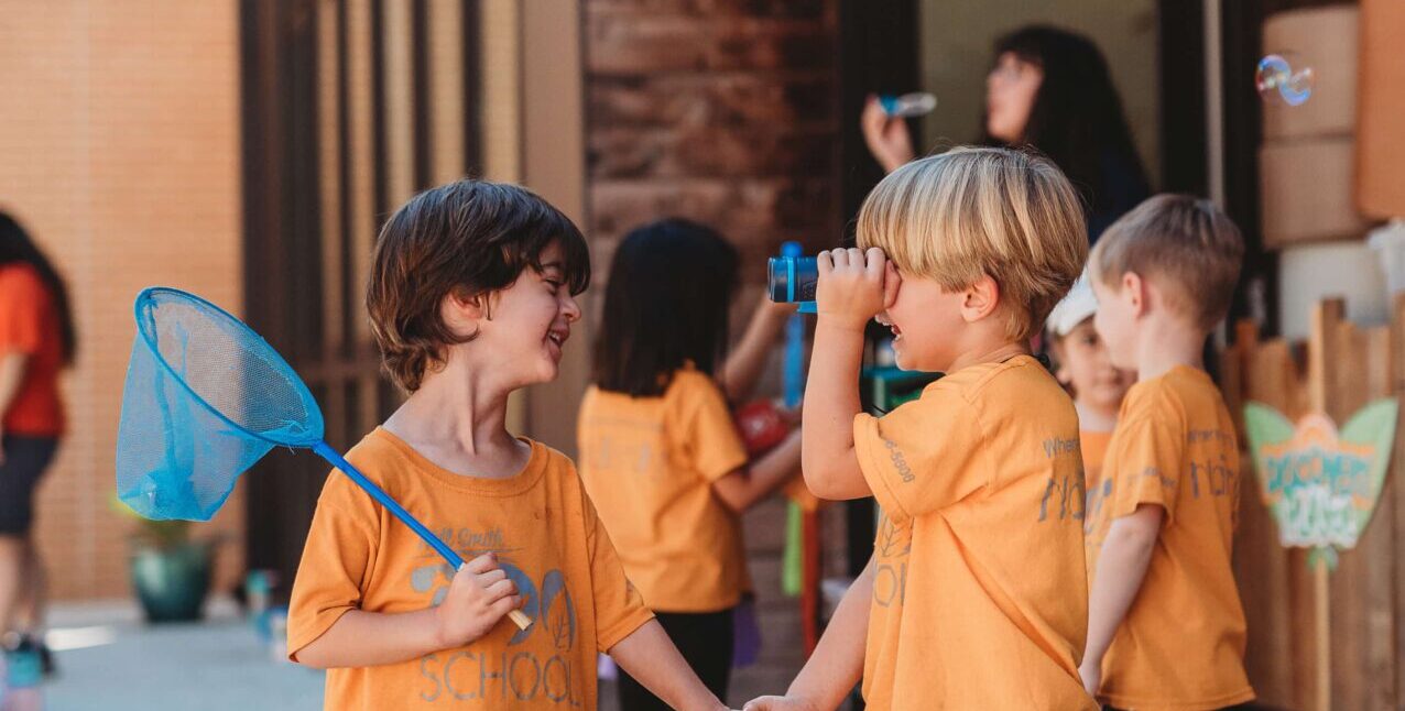 Two young boys in orange shirts holding hands and playing at the Zoo School