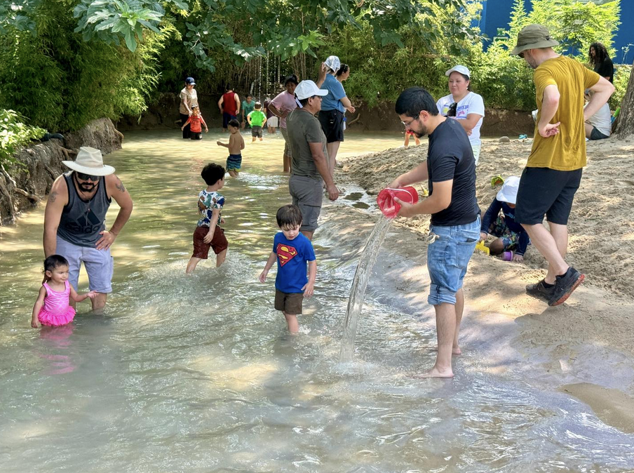 Children playing in a shallow stream near a turtle sculpture at the water play area in the San Antonio Zoo