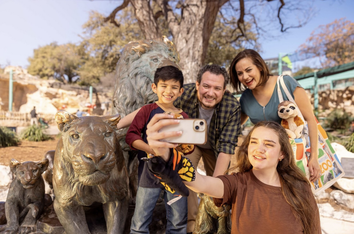 A family posing for a selfie next to a bronze lion statue at the San Antonio Zoo