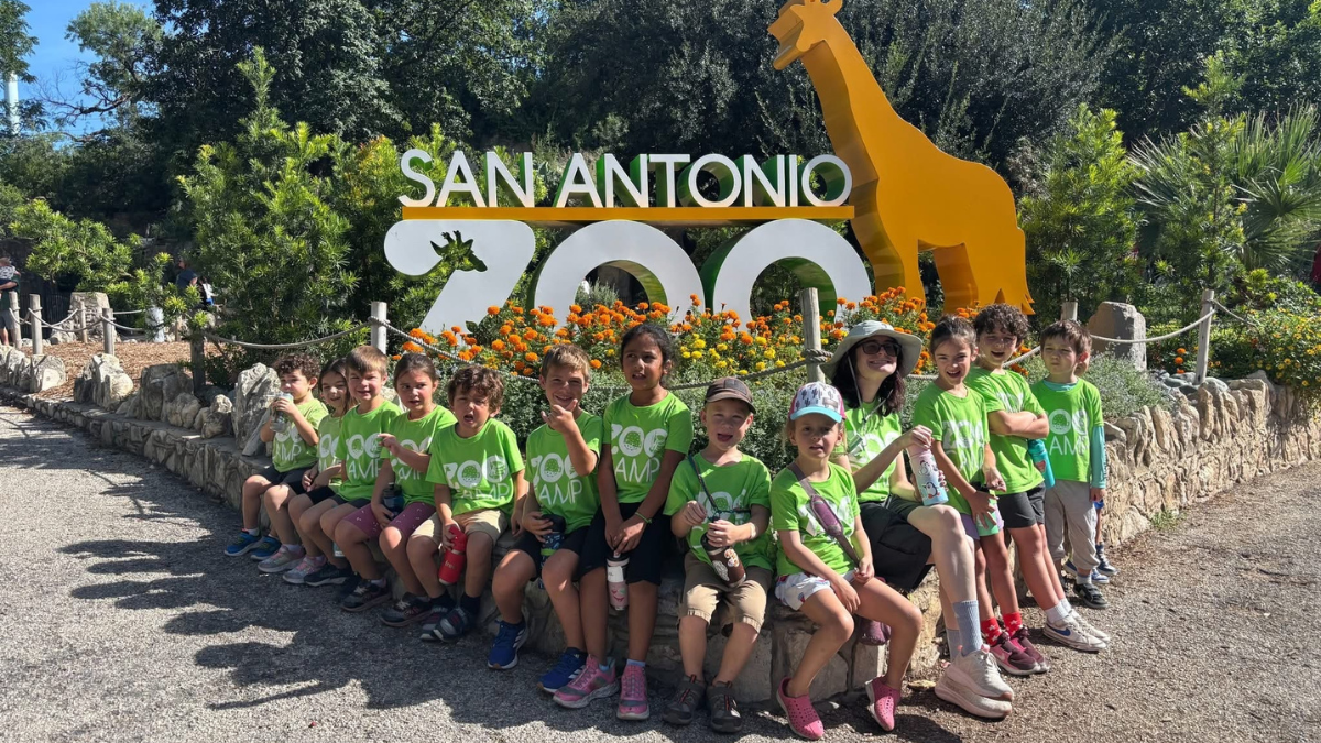 San Antonio Zoo Camp group photo in front of the San Antonio Zoo entrance sign with giraffe sculpture