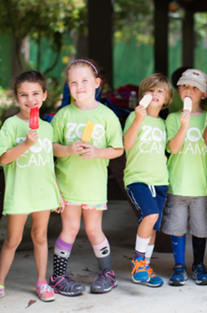 Kids in San Antonio Zoo Camp shirts enjoy popsicles together during a summer camp break outdoors